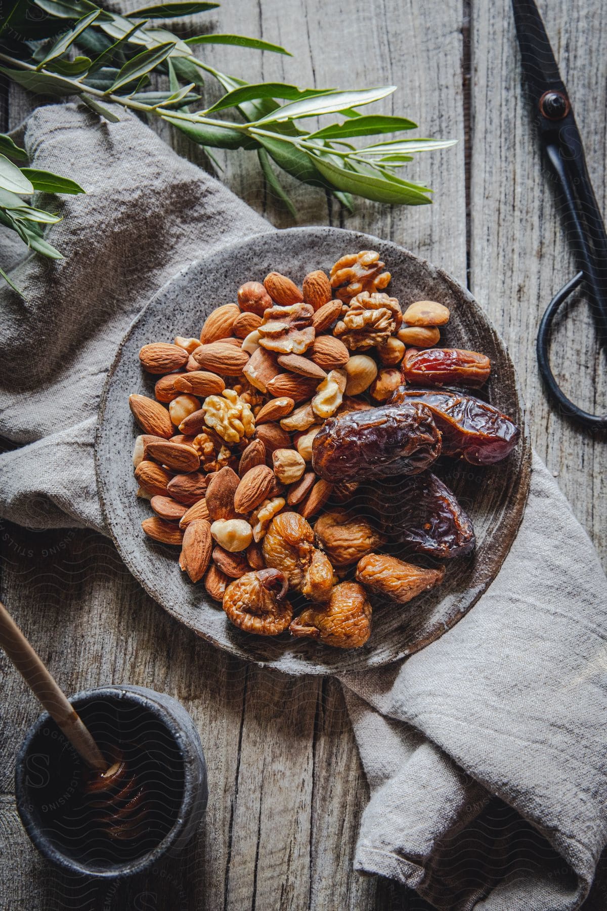 Stock photo of a plate of different types of nuts and a container of honey are placed on a piece of towel cloth