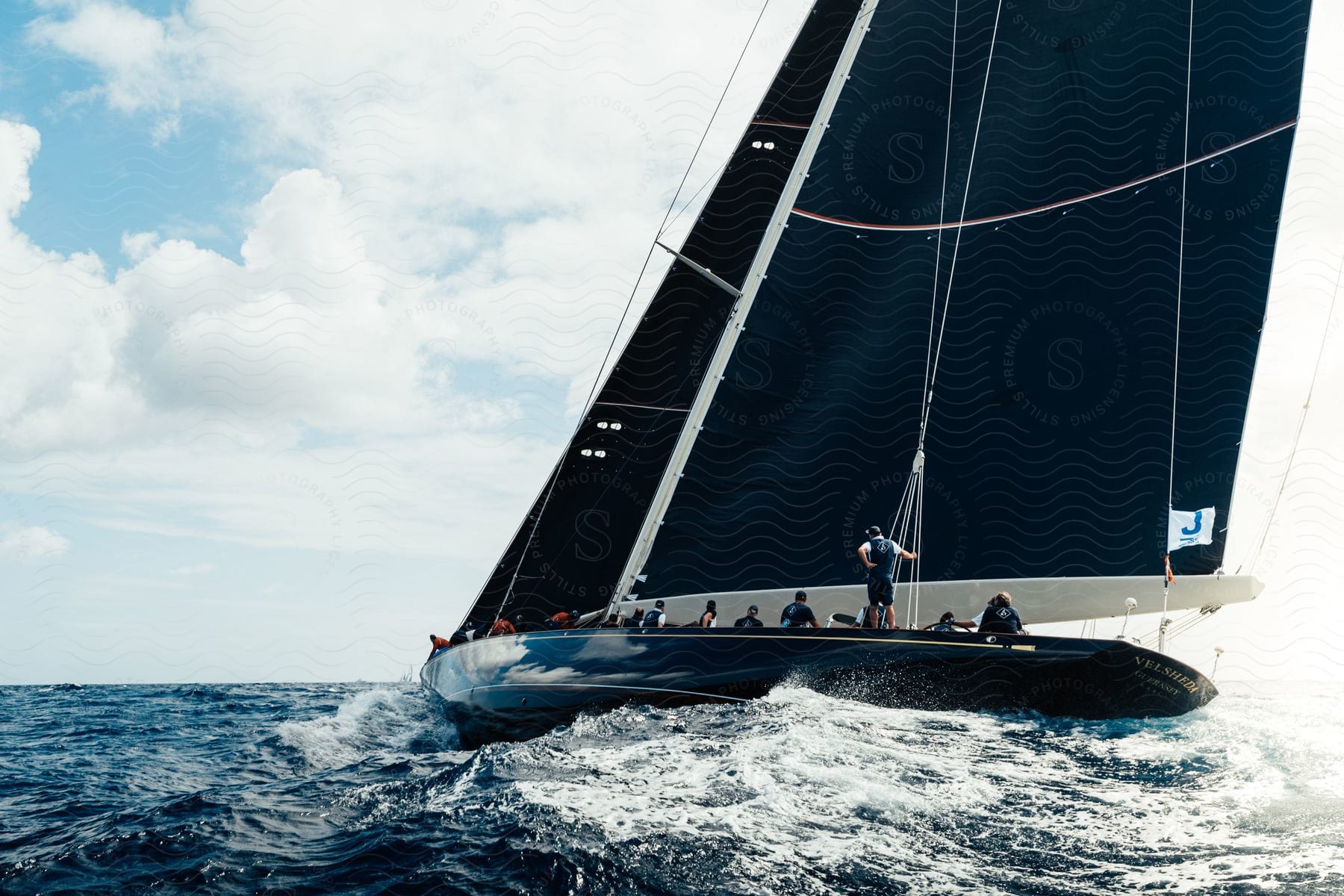 A crew of people sit on a sailboat in the middle of the sea during the day