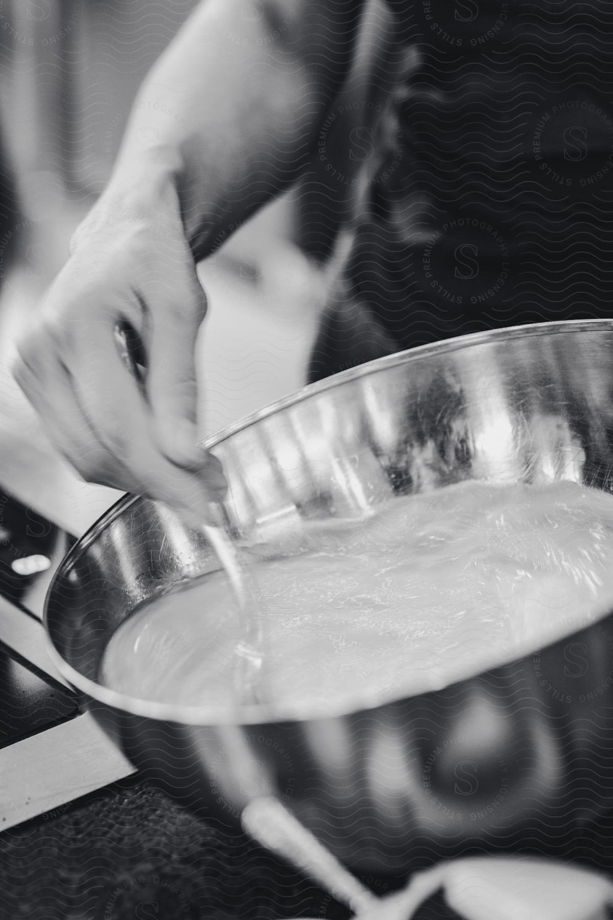 A closeup of a silver mixing bowl with dough being mixed by a man