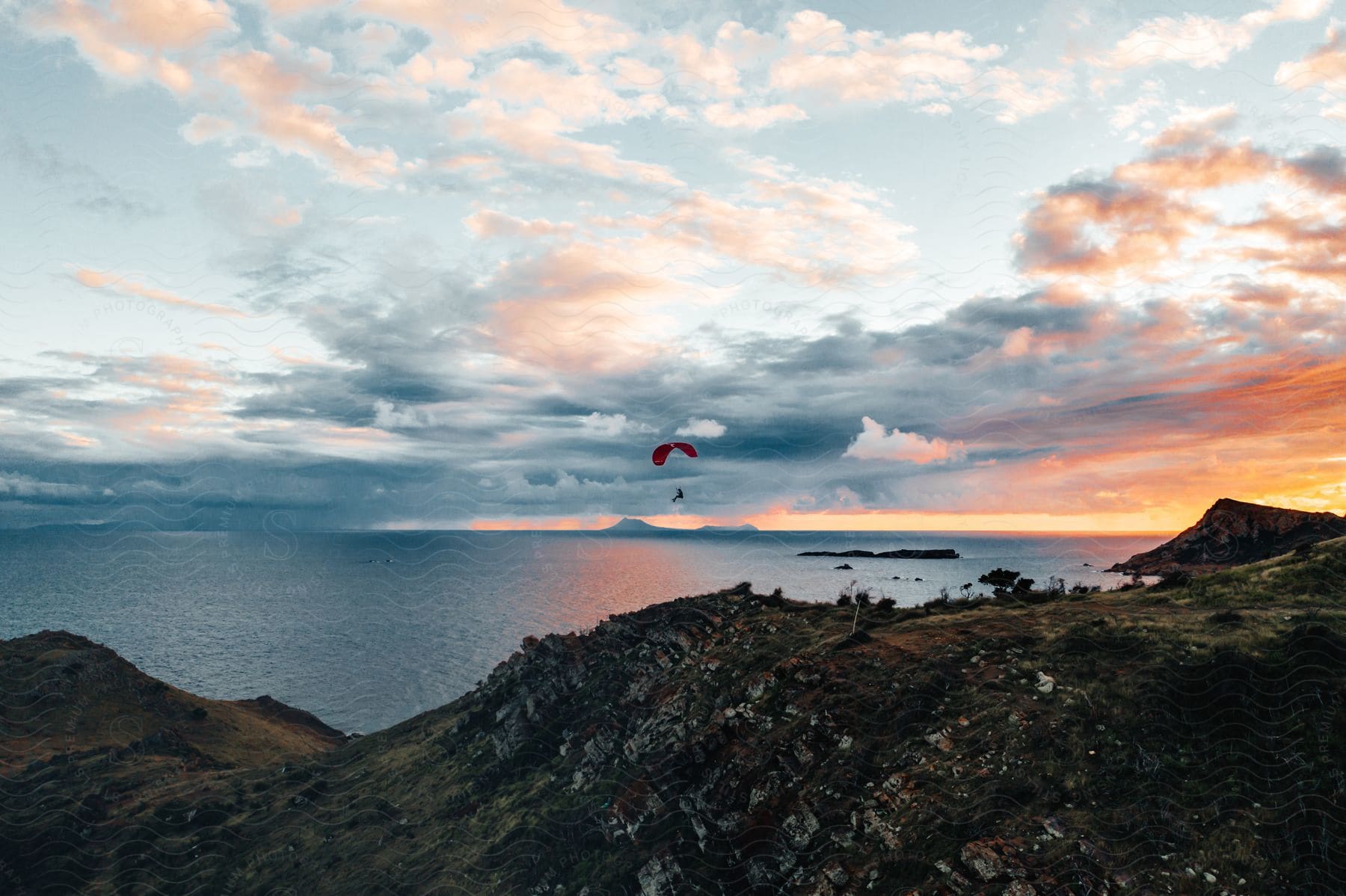 A colorful cloud formation fills the sky over rolling hills as a person glides through the air