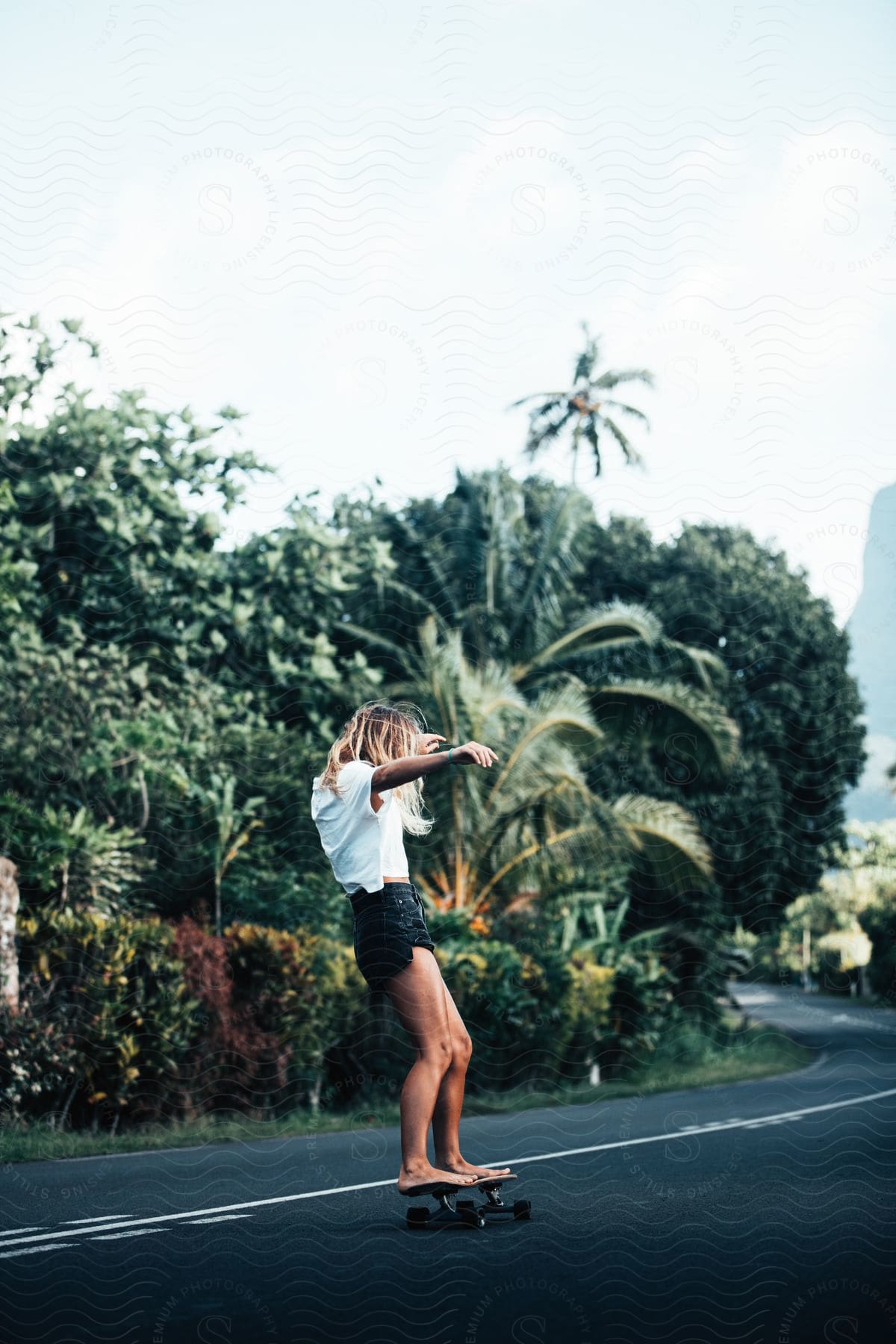 A person skateboarding on asphalt with trees and sky in the background