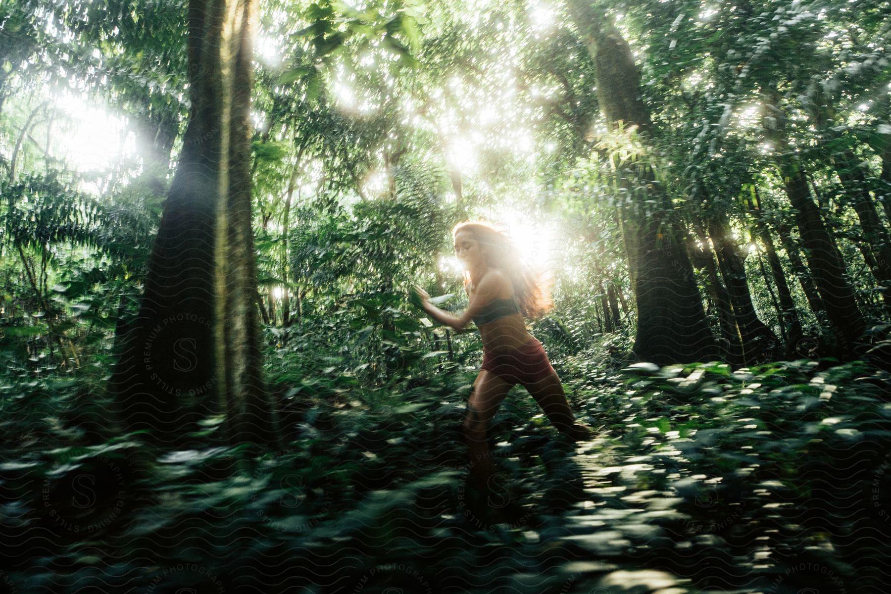 Woman with brown hair green sports bra and red shorts running in a green forest