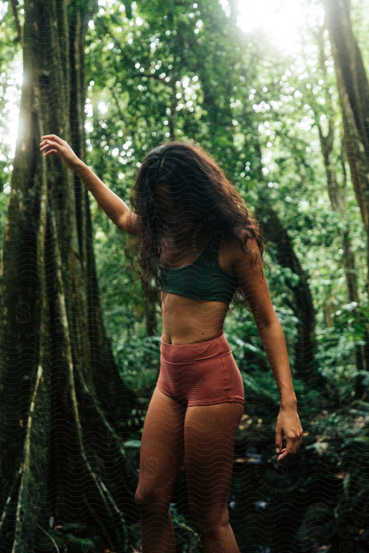 A woman with dark wavy hair green bra and red shorts walks in the jungle