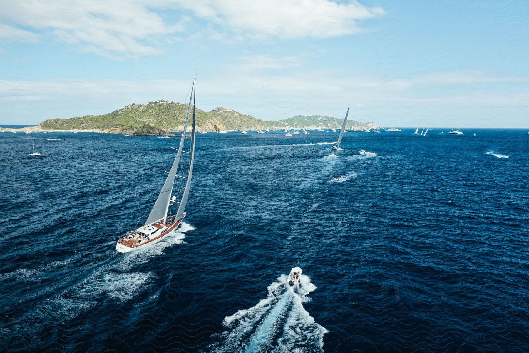 Sailboat and motorboat surrounded by other boats with the coast in the background on the sea