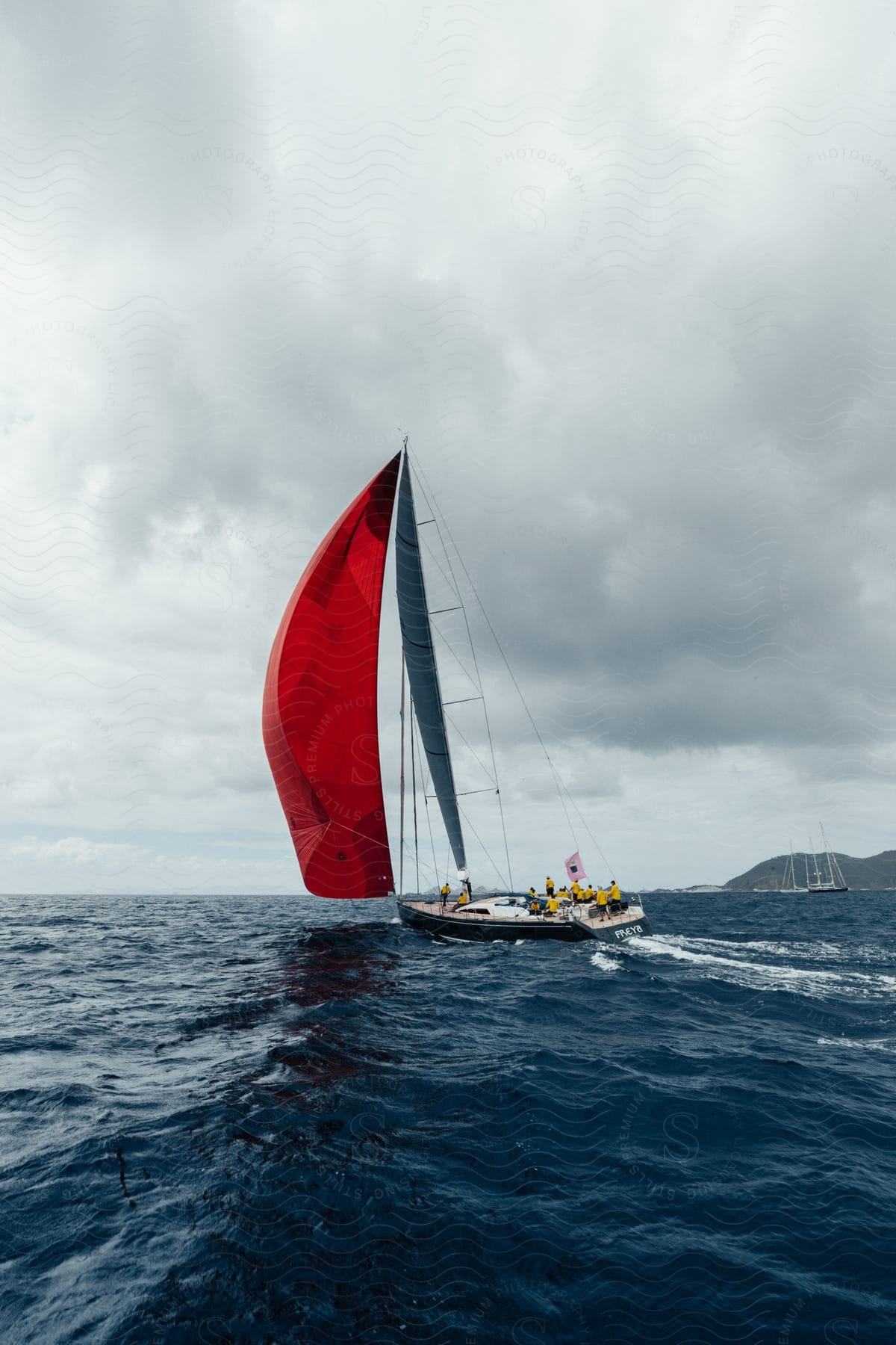 A sailboat crew navigates choppy waters on a cloudy day