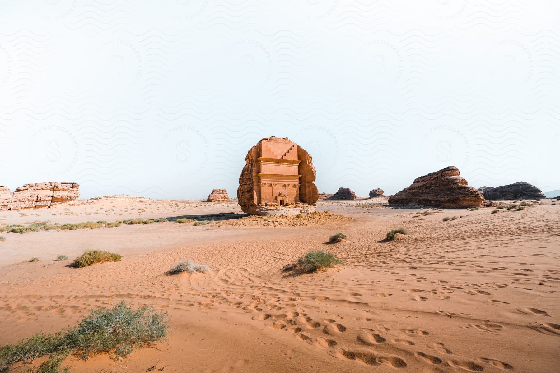 A desert with a crumbling structure scattered rocks footprints in the sand and sparse vegetation is home to various rock formations