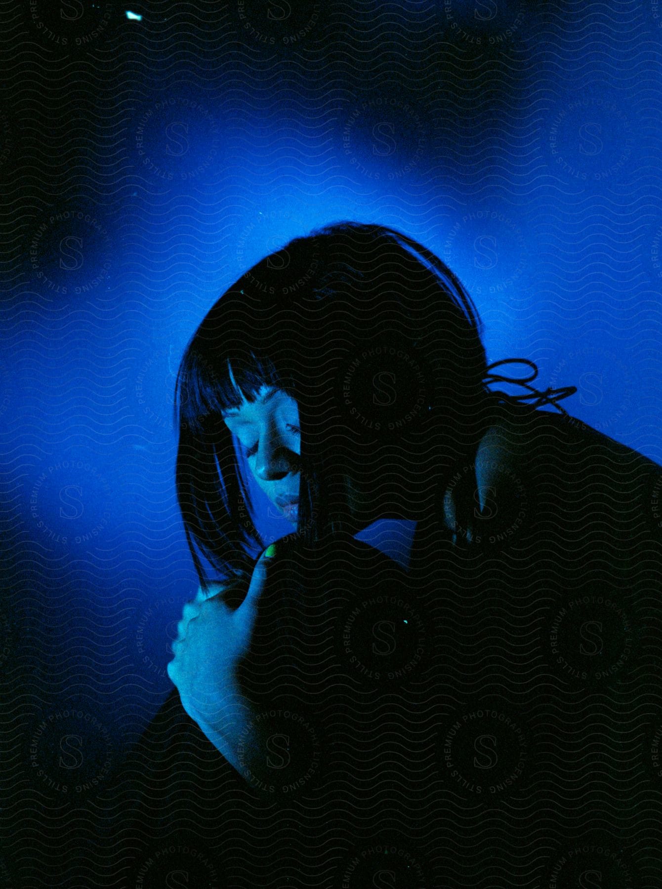 Woman with bob hair and eyes closed is surrounded by blue and black lights in the studio