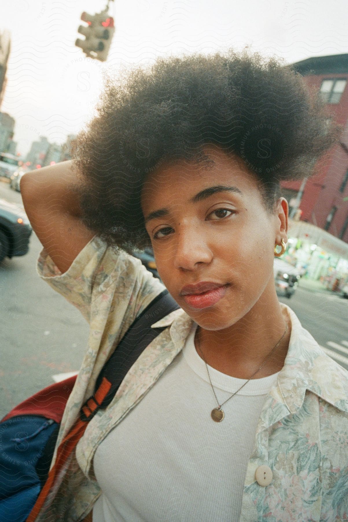 Curlyhaired girl with earrings and backpack smiles on city street