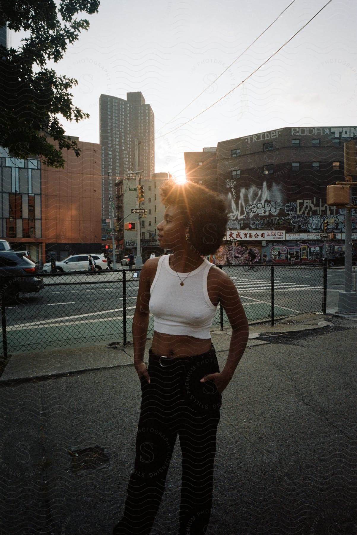 Woman standing on street corner during sunset in urban setting with light traffic