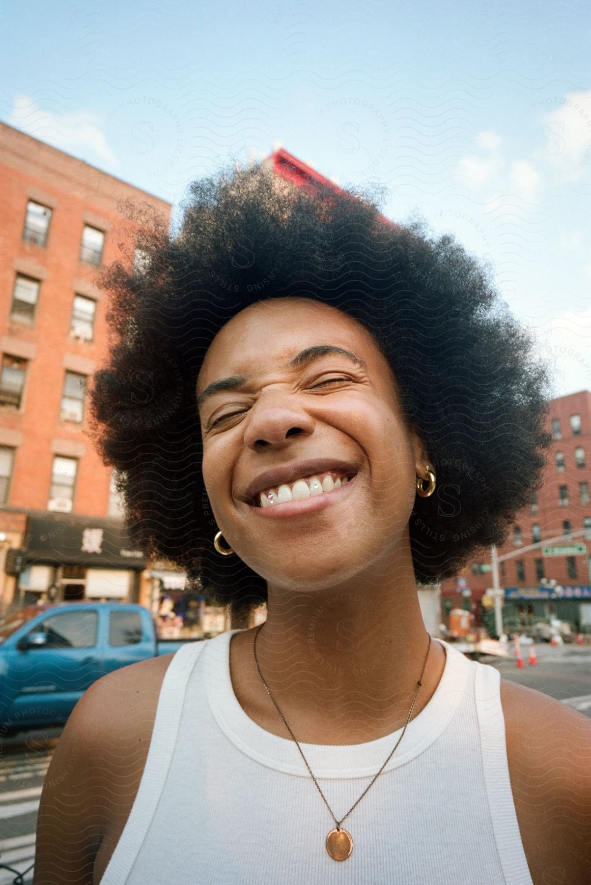 Woman with curly hair earrings and white sleeveless shirt smiling broadly on the street in downtown nyc