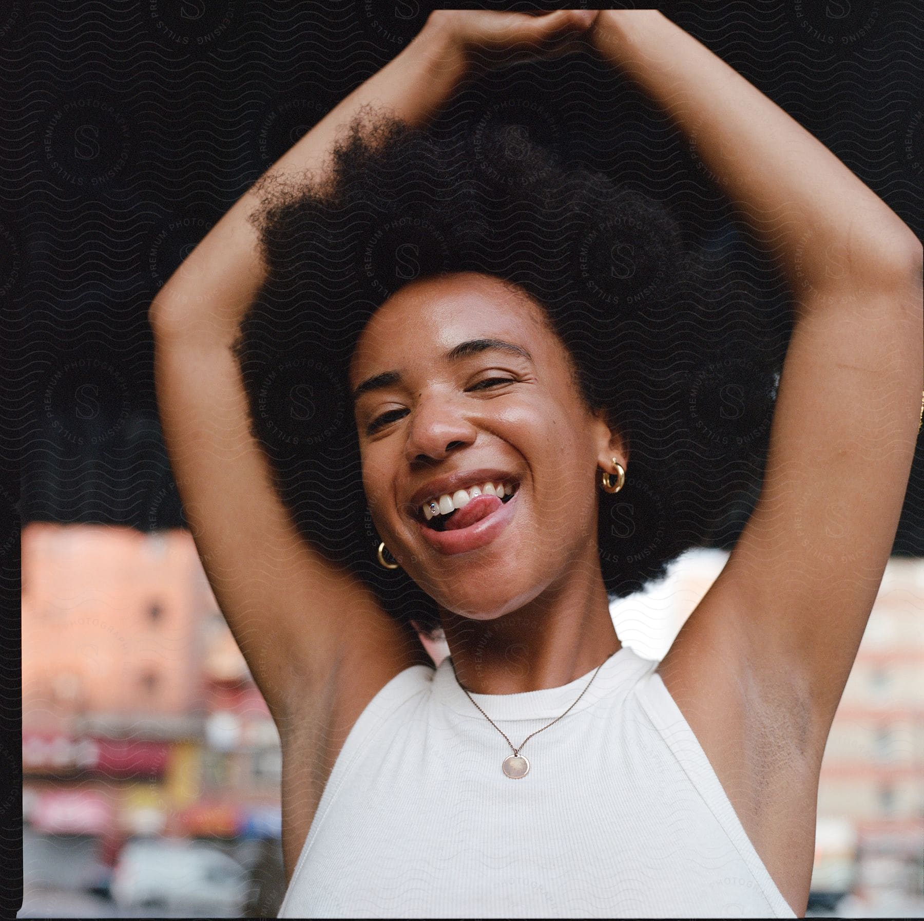 A young woman wearing a white sleeveless shirt holds her hands above her head