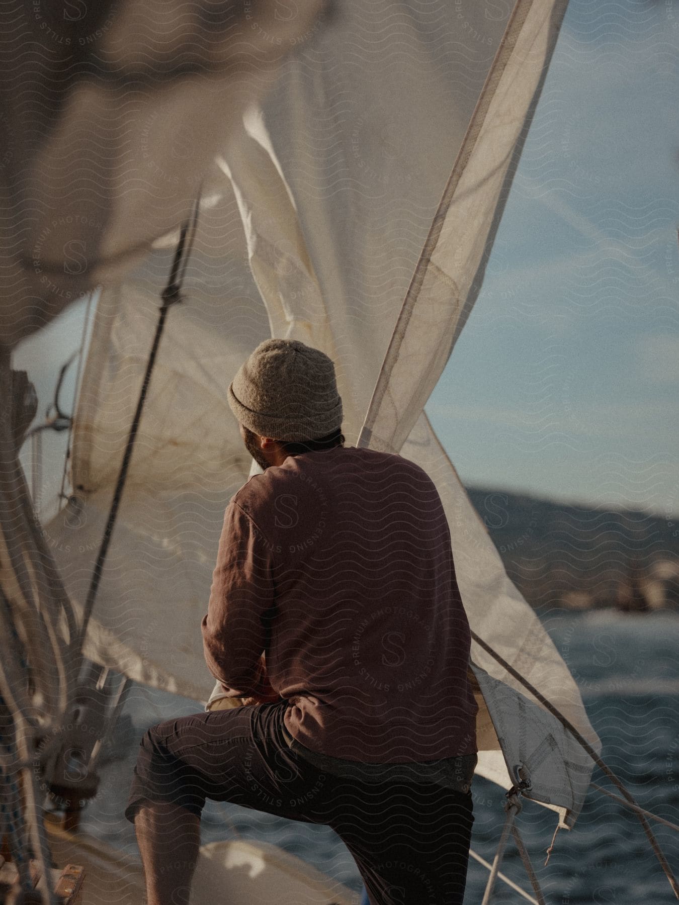 A man standing in a sailboat near the coast in the evening