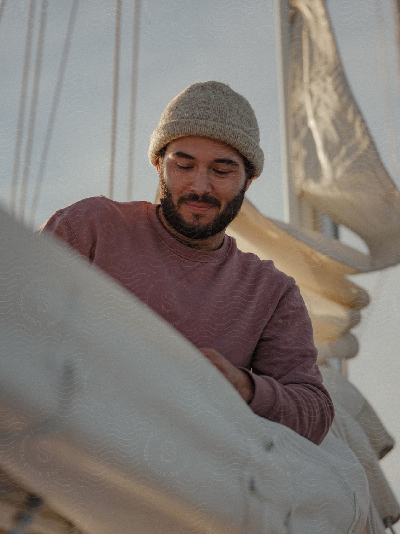 Man on sailboat smiles slightly while working with sail