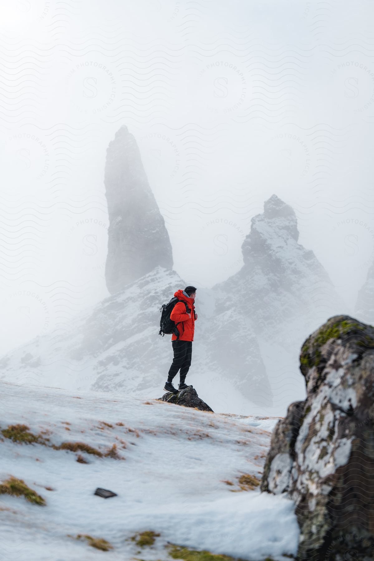A hiker stands on a snowcovered mountainside near tall rock formations wearing a backpack