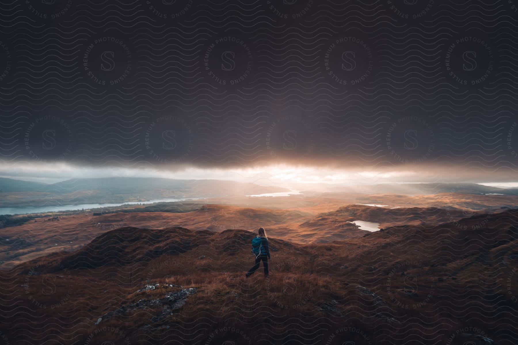 A person gazes at dark clouds on the horizon from the top of a mountain range