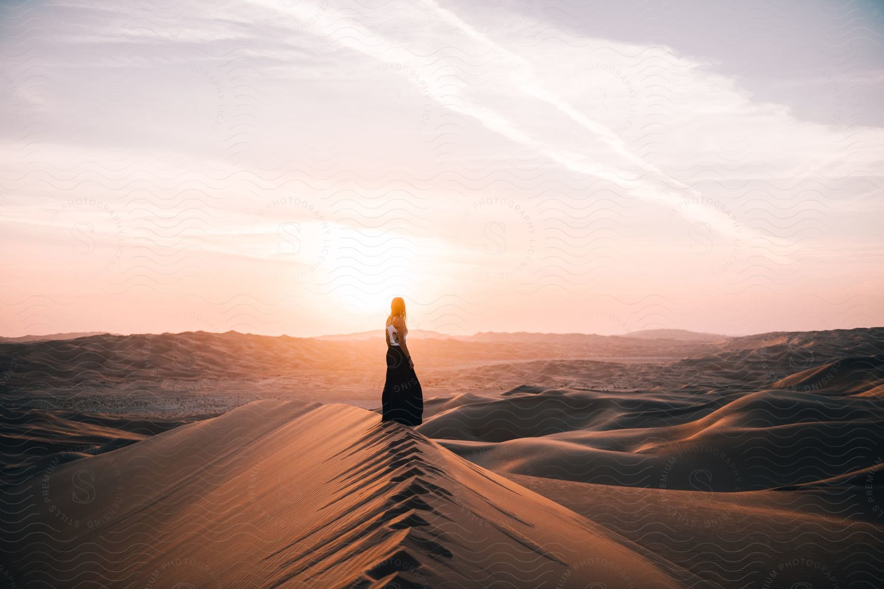 A woman standing on a sand dune in the desert at dawn