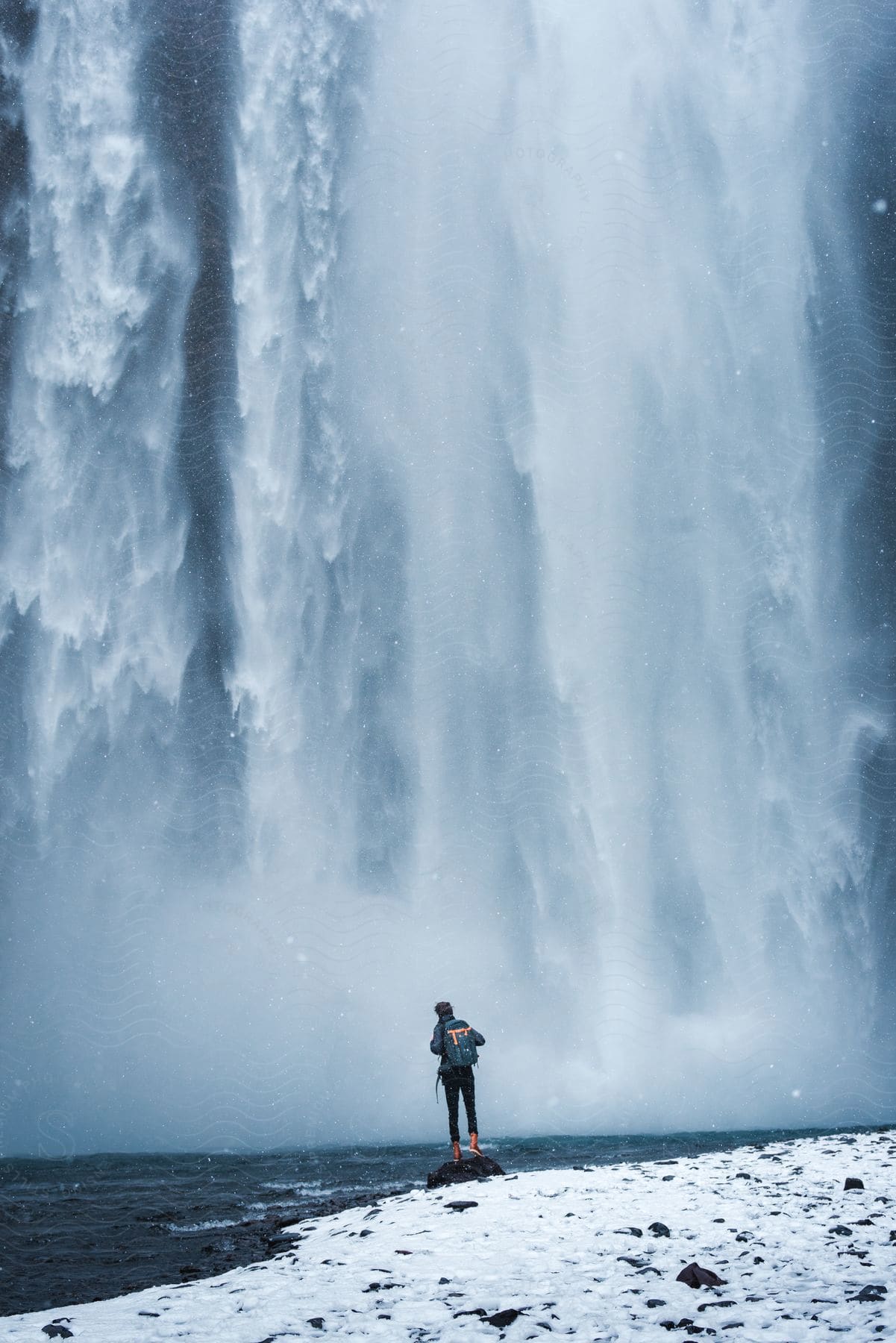 A backpackwearing tourist stands near a magnificent waterfall in iceland admiring the breathtaking scenery