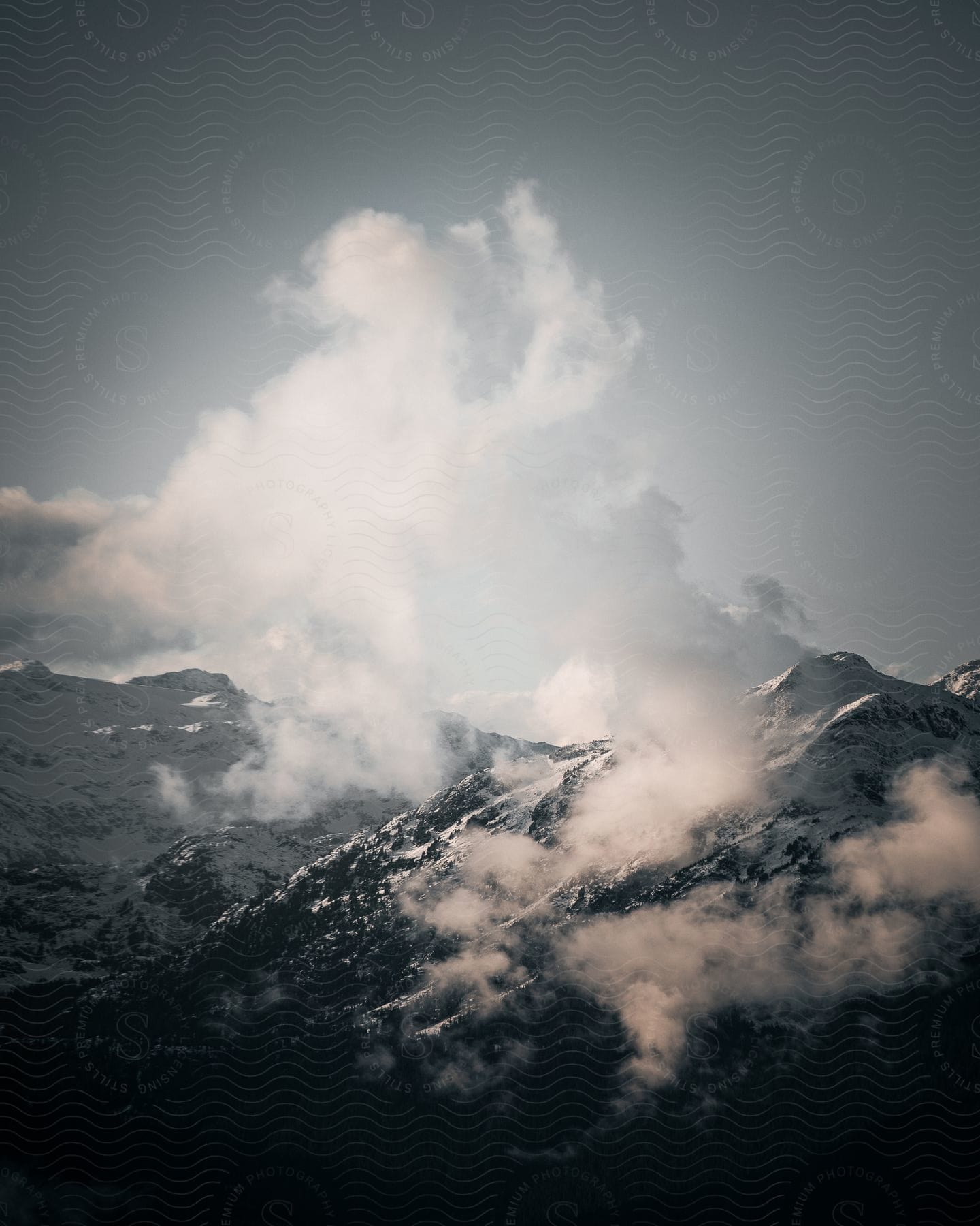 A tall mountain top with ice capped points and foglike substance near the peaks