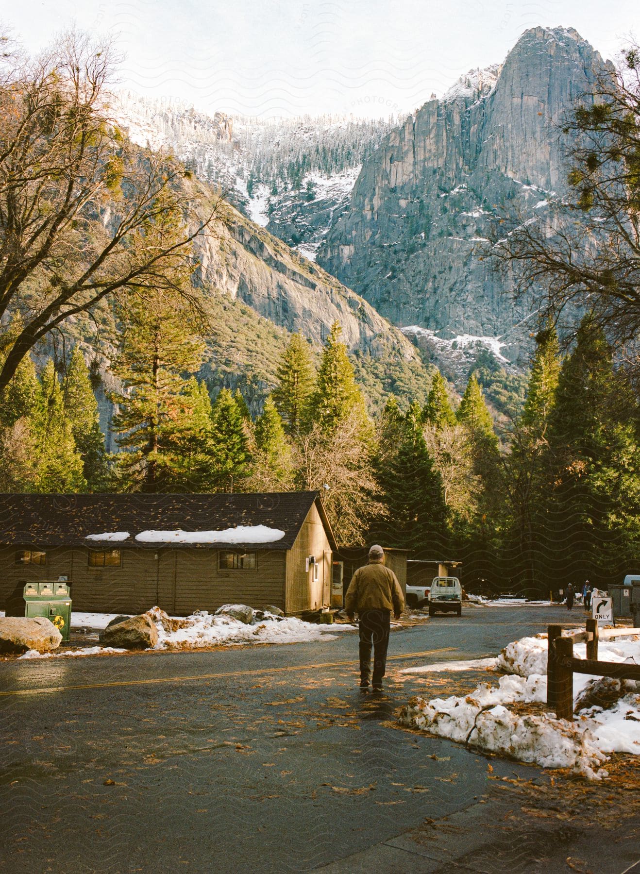 A man walks down a street in a small town at the base of snowy mountains