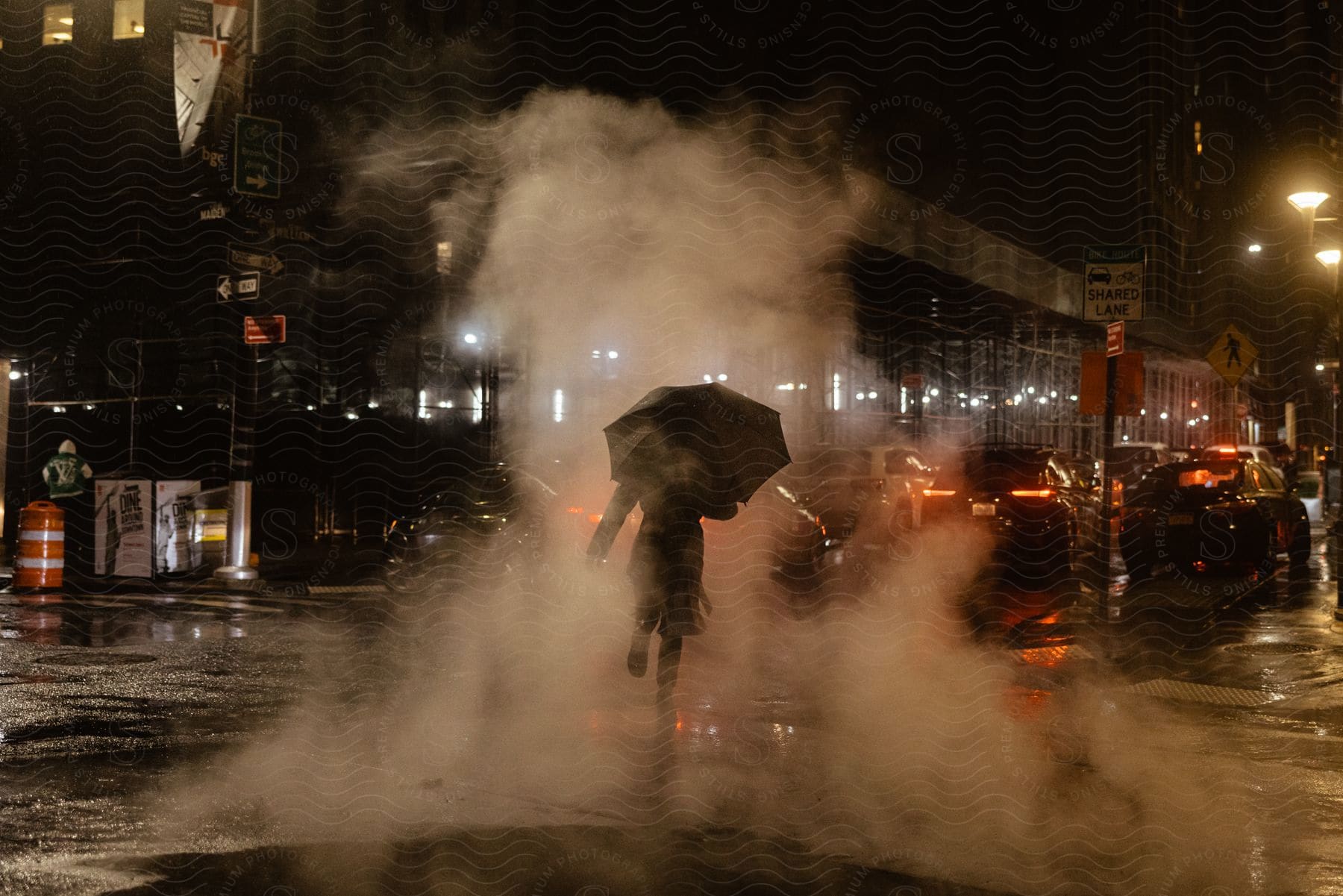 A person with an umbrella runs through fog in a big city at night