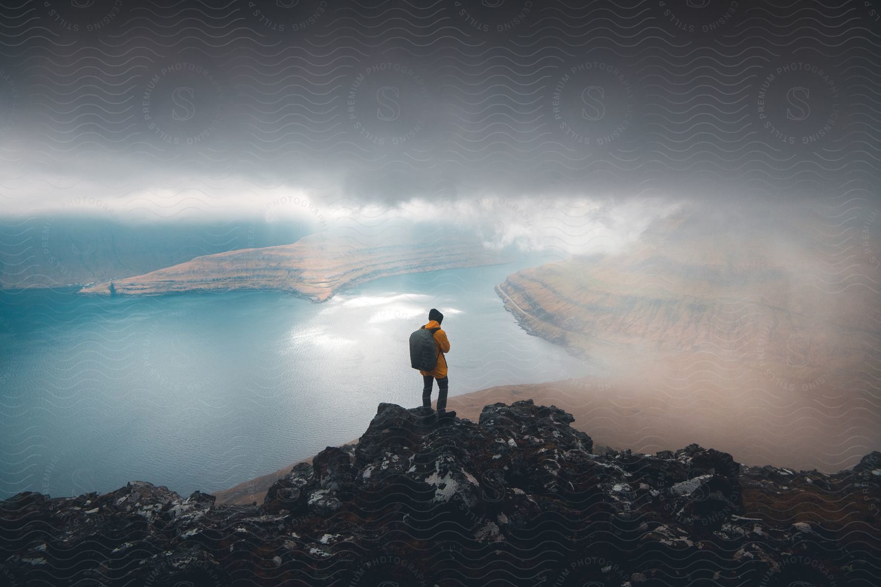 A person standing on a cliff overlooking water and mountains in the faroe islands