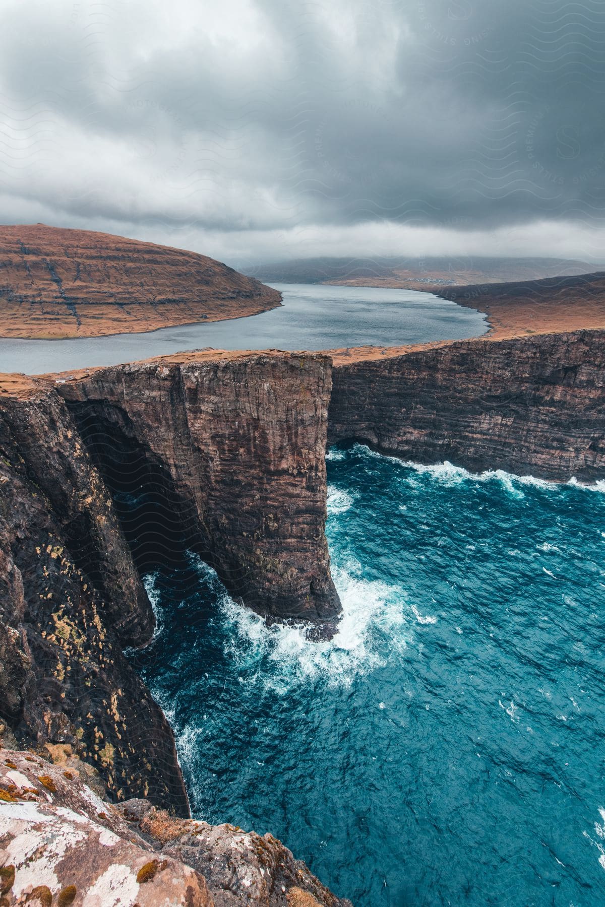 River flowing around hilltop with waterfall between cliffs on cloudy day