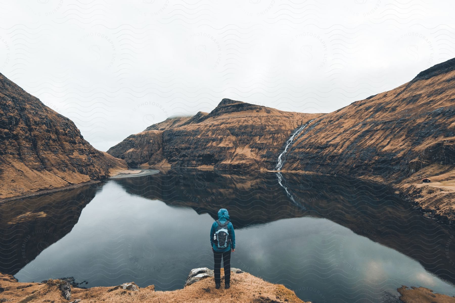 A person standing at the edge of a lake wearing a coat and backpack