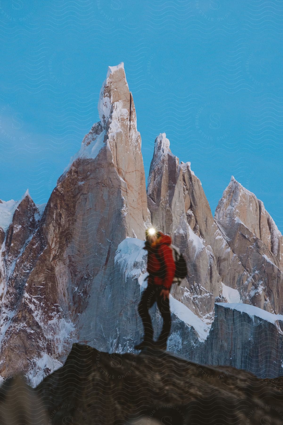 A man with a red jacket hiking on a mountain with a backpack