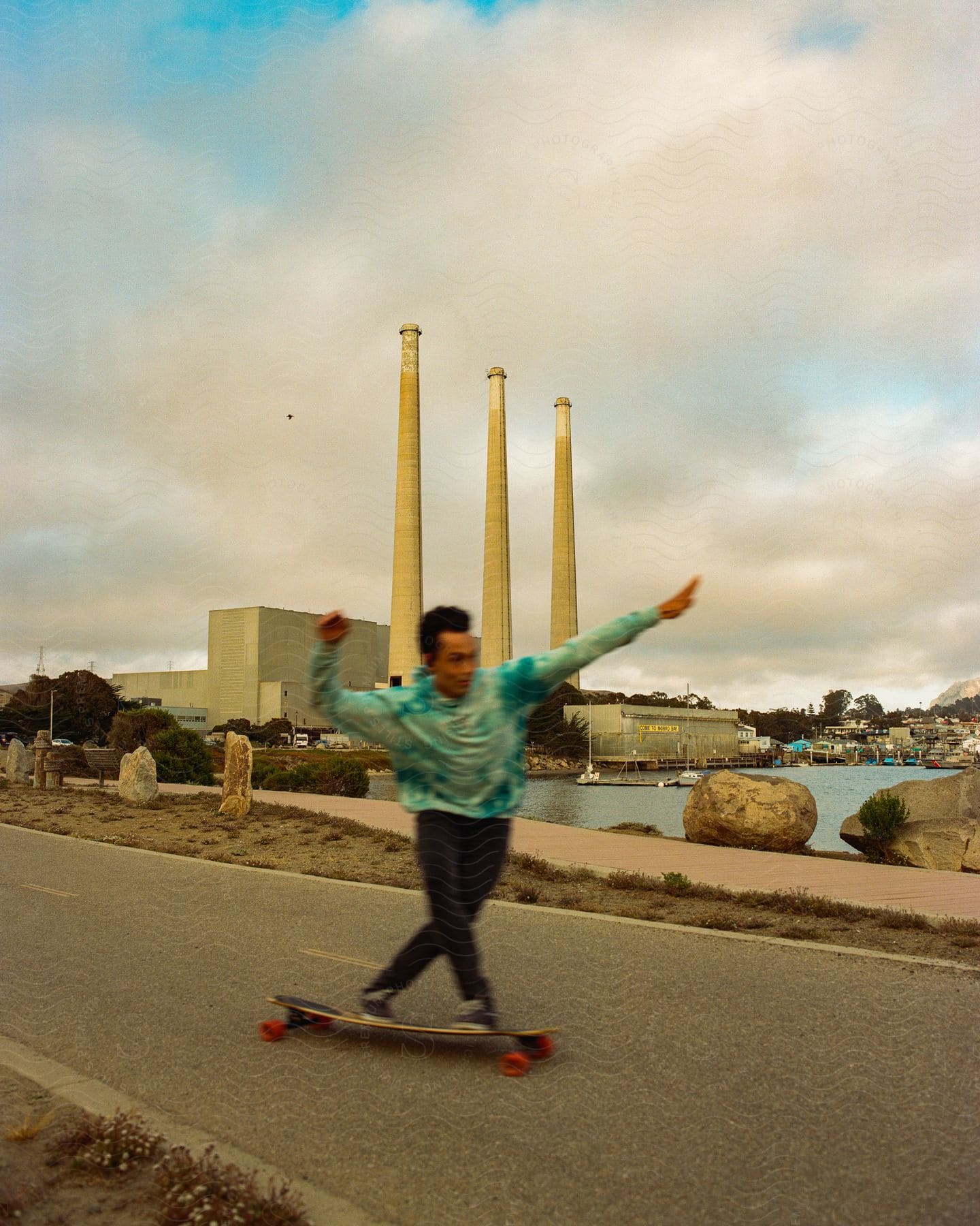 A man confidently skiing on a board along a street with a river and buildings beside him