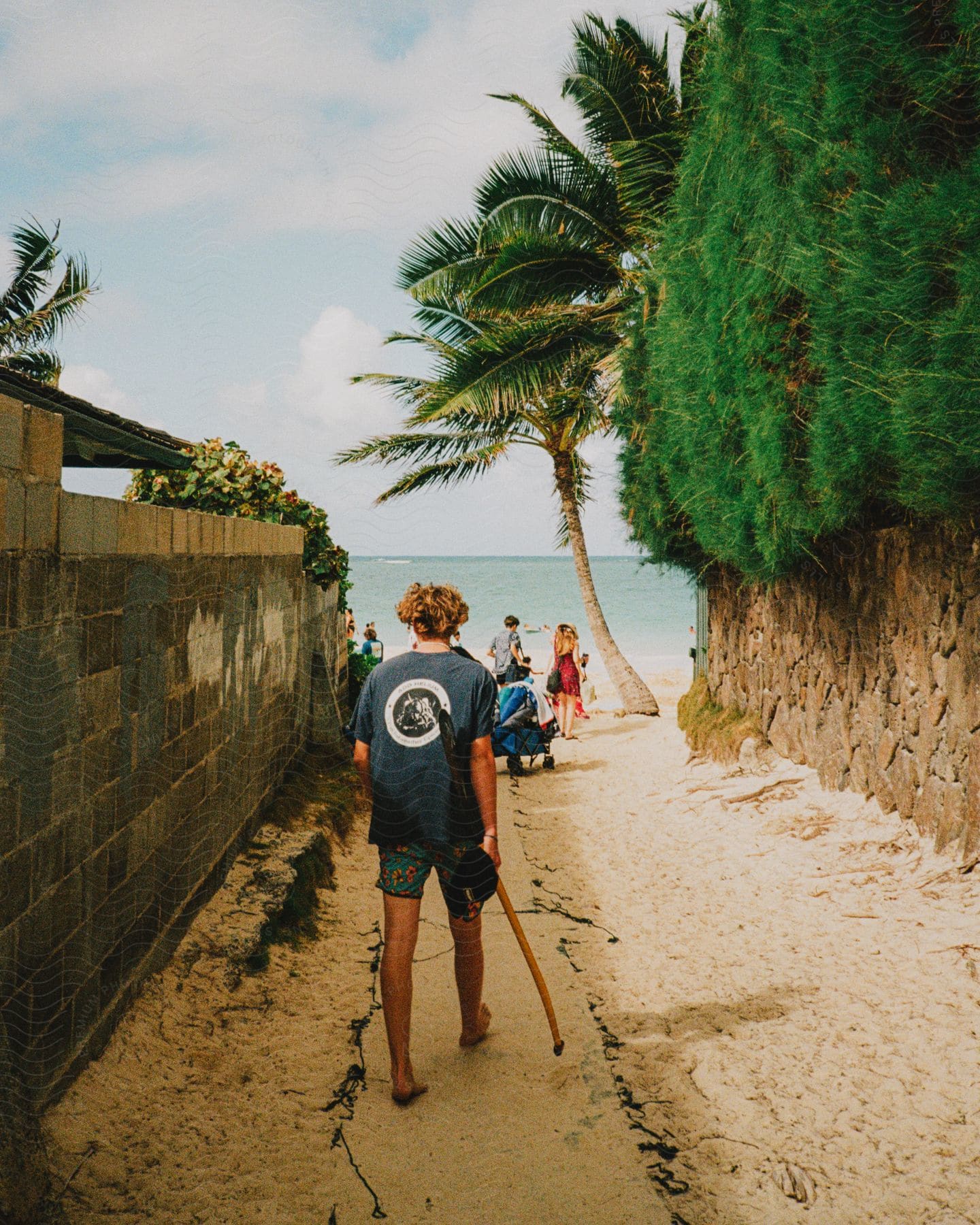 A person walking on a sandy path towards a beach where other people are already standing