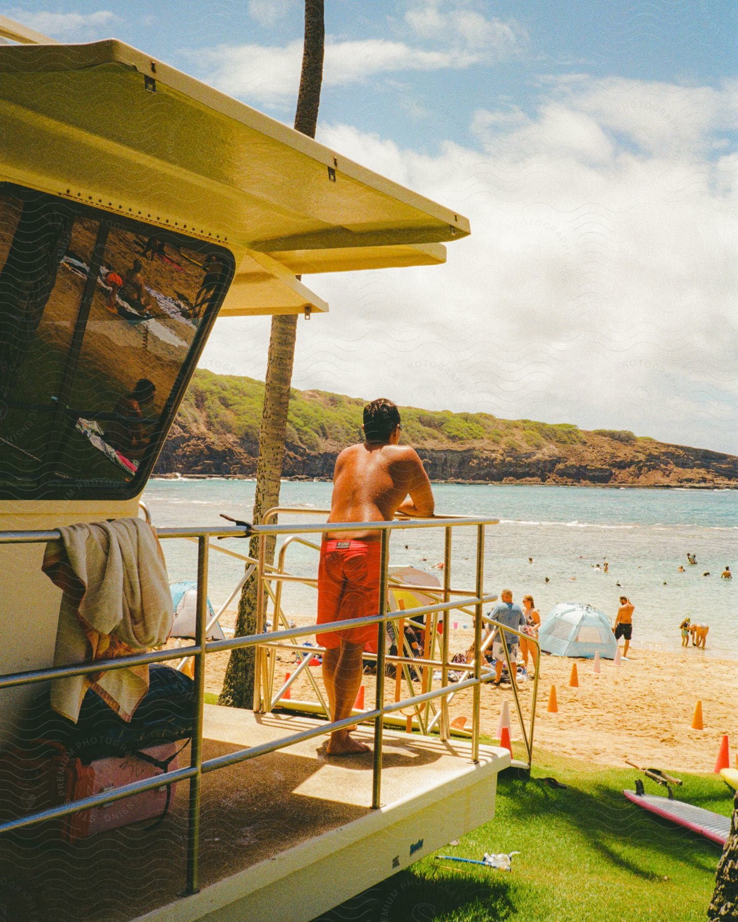 A man standing in a beach house observing people playing on the beach during the day
