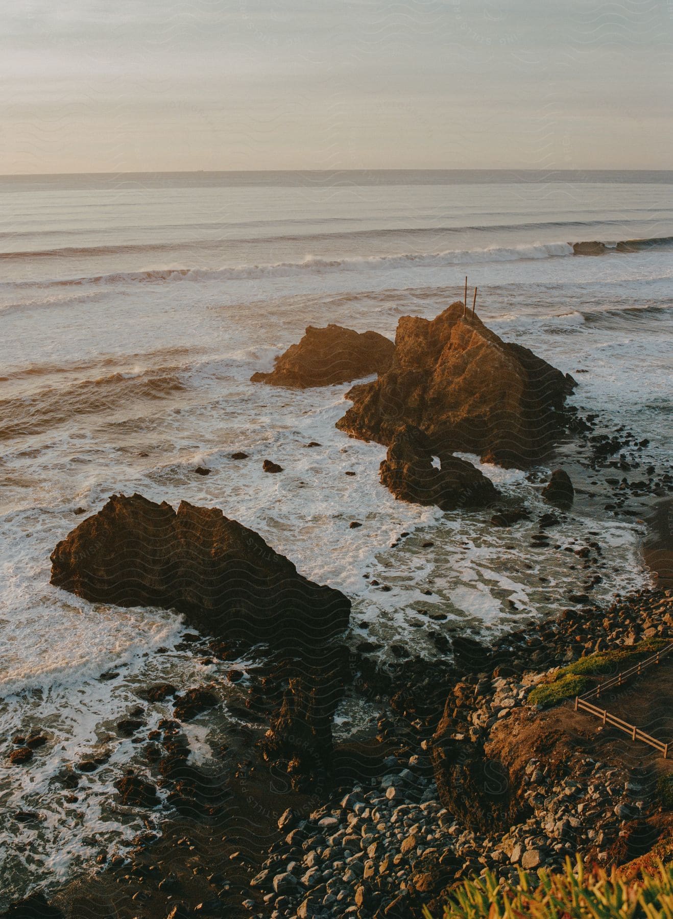 The ocean waves crash into rocks under a blue sky