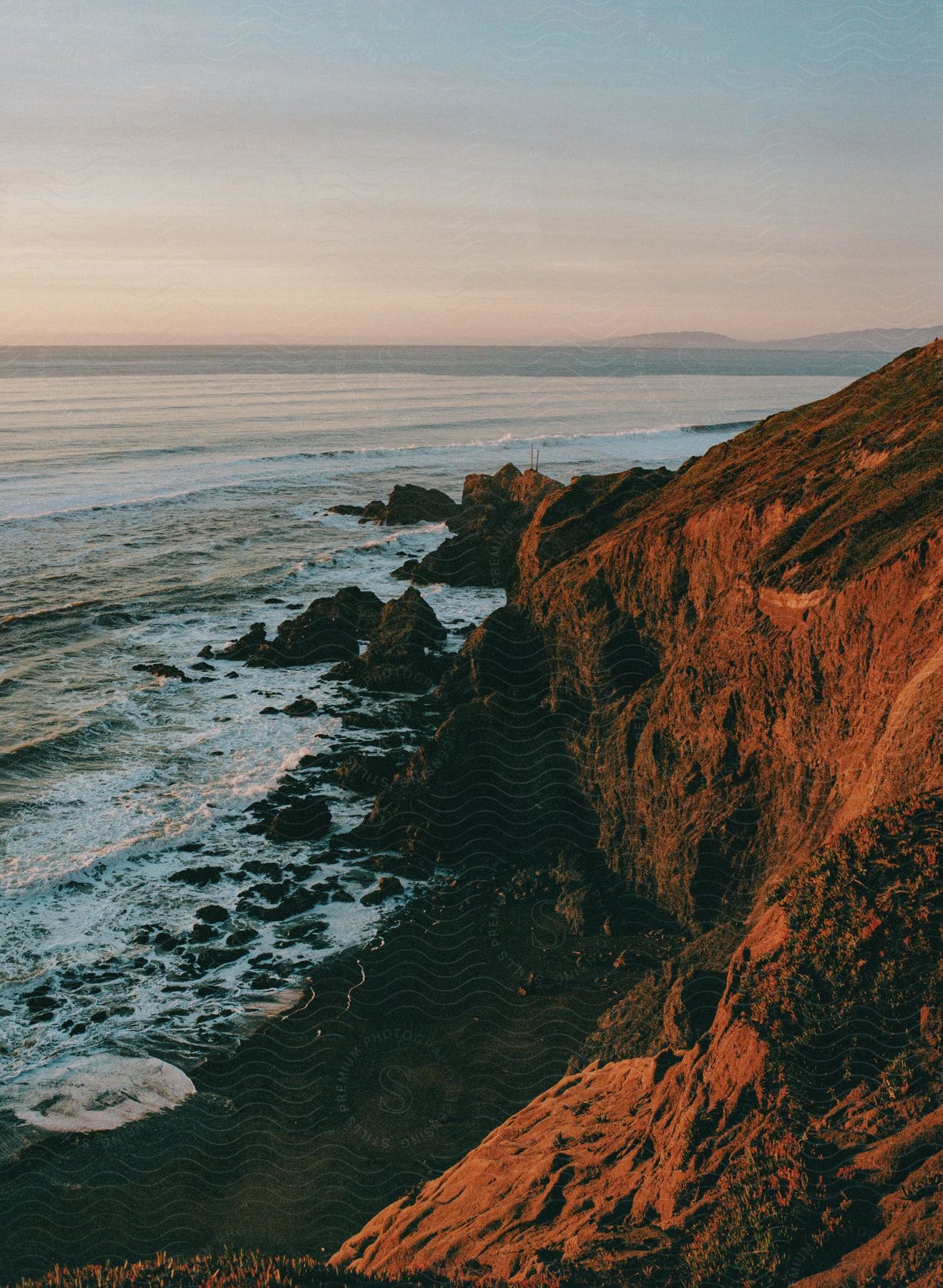 Waves splash against rocks along the coast with distant mountains