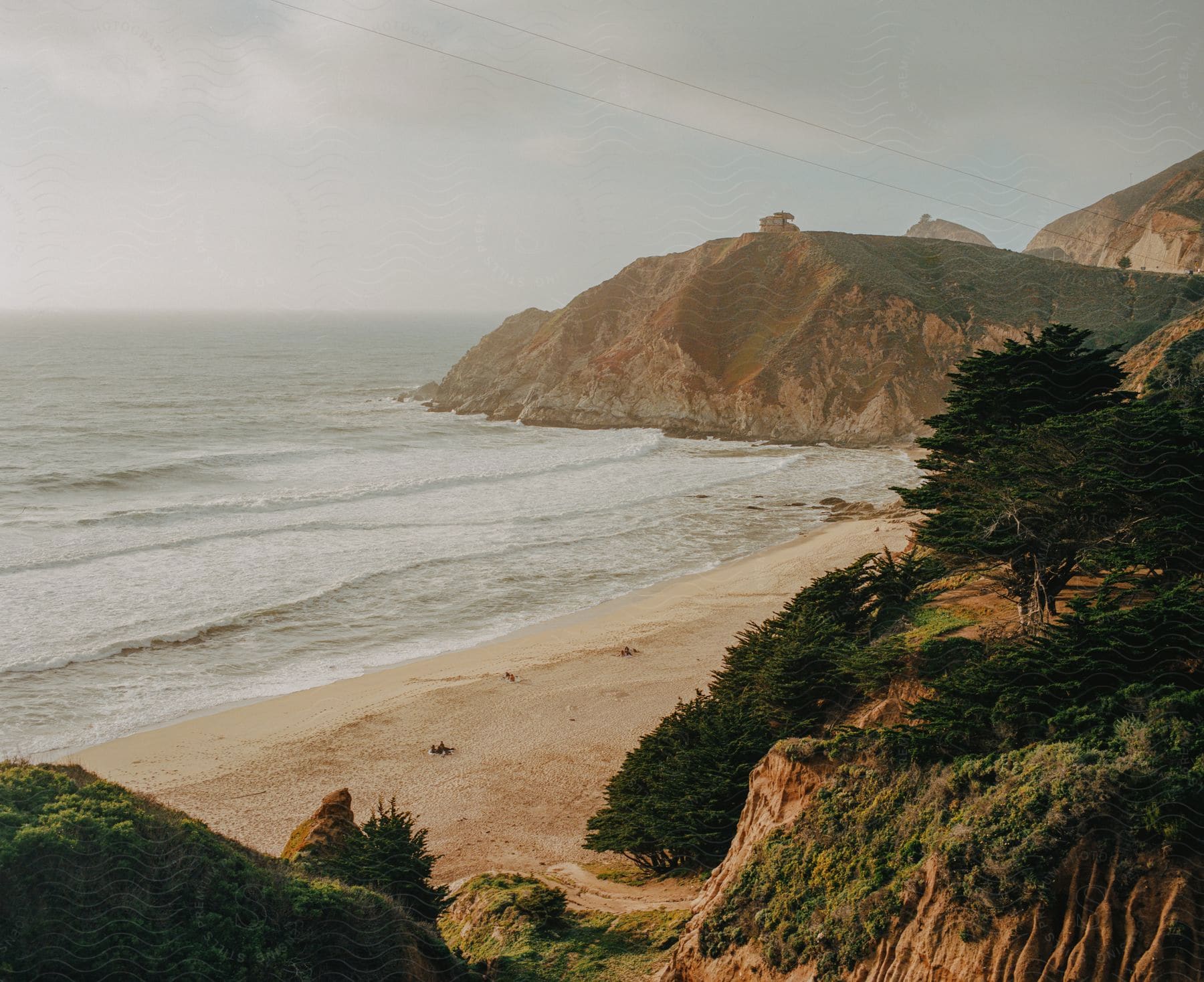 Waves roll into shore over a beach with trees on a plateau and a promontory along the coast