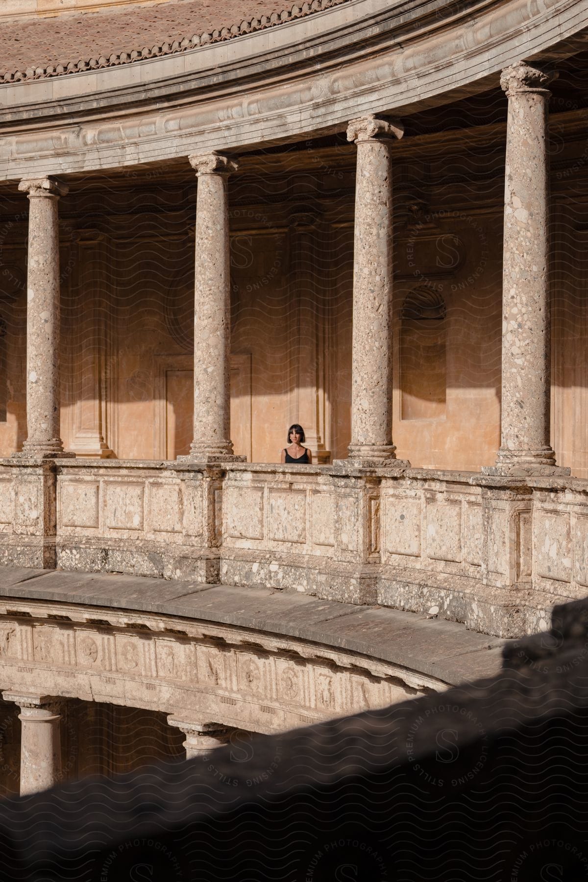 A young woman is standing outside on the upper level of an old colosseum.