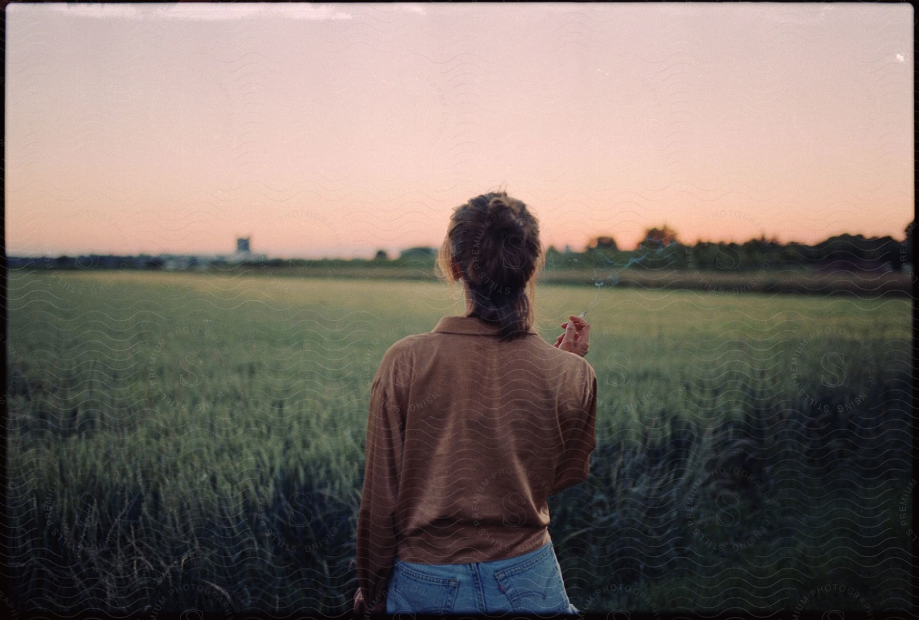 Woman smoking a cigarette outdoors next to a large crop field at dusk