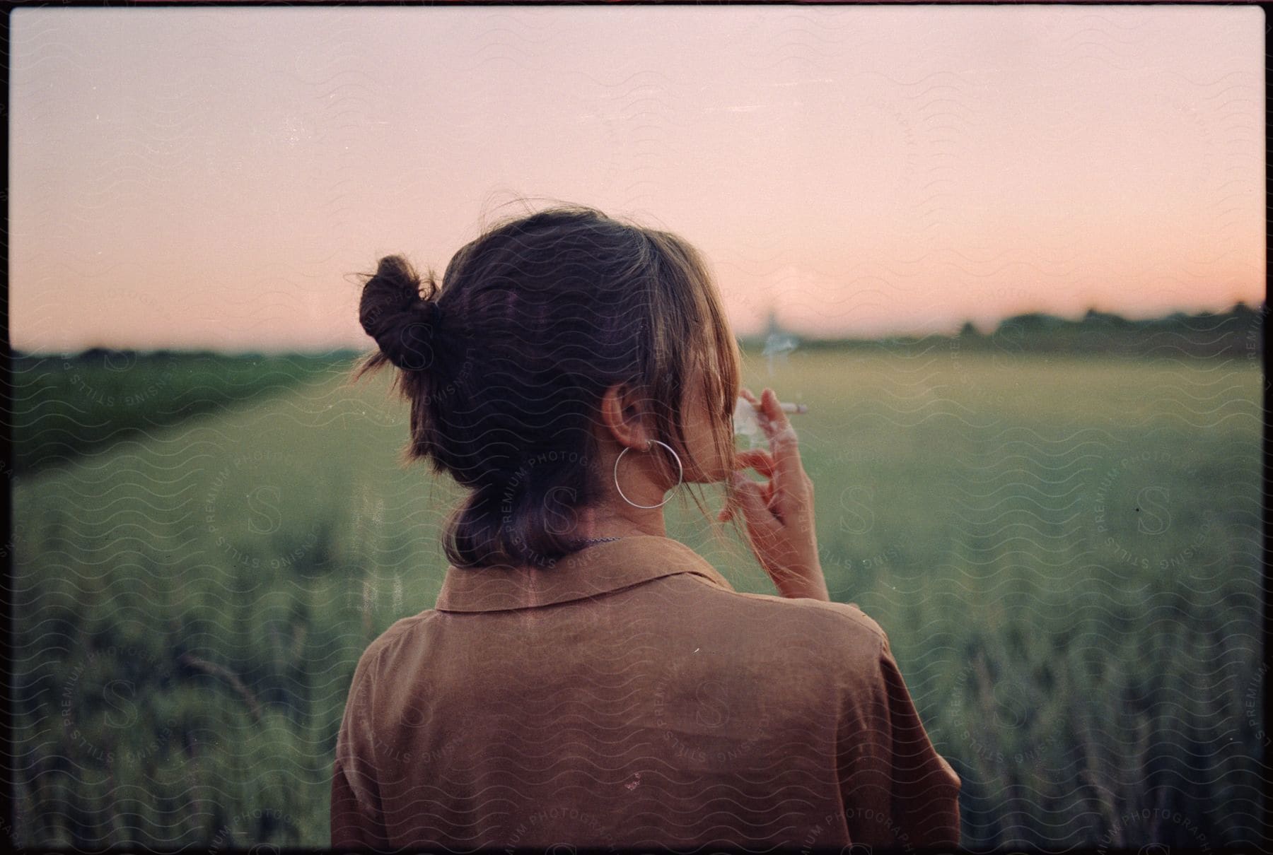 Woman smoking a cigarette outside next to a grass field