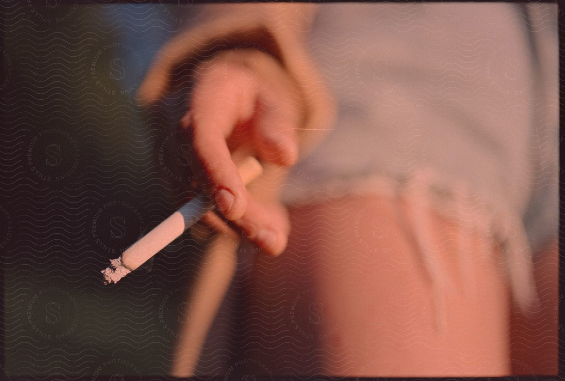 A woman wearing denim shorts shakes ash off a cigarette between her fingers