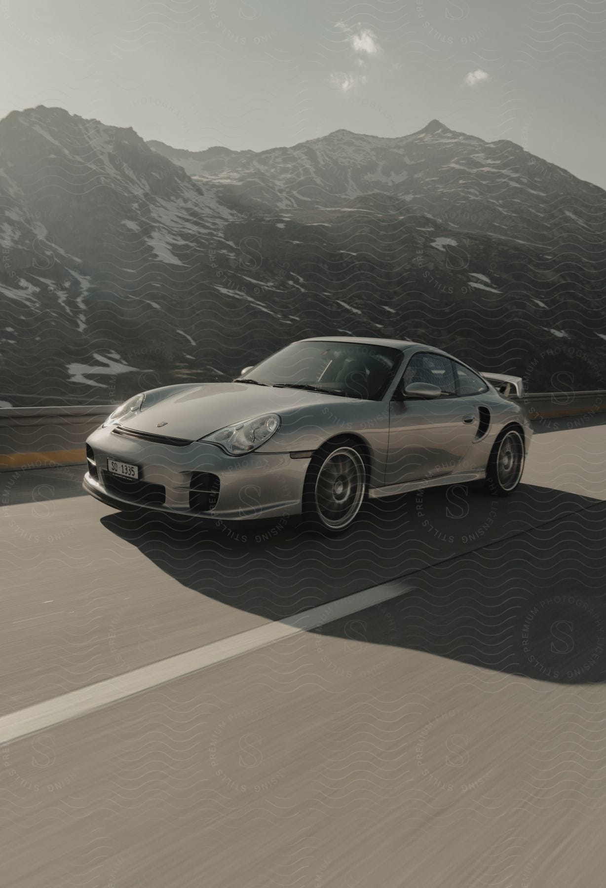 A sports car drives on a highway with snow mountains in the background