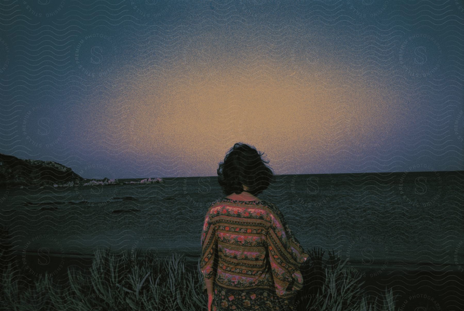 A young girl stands outside looking out over the ocean