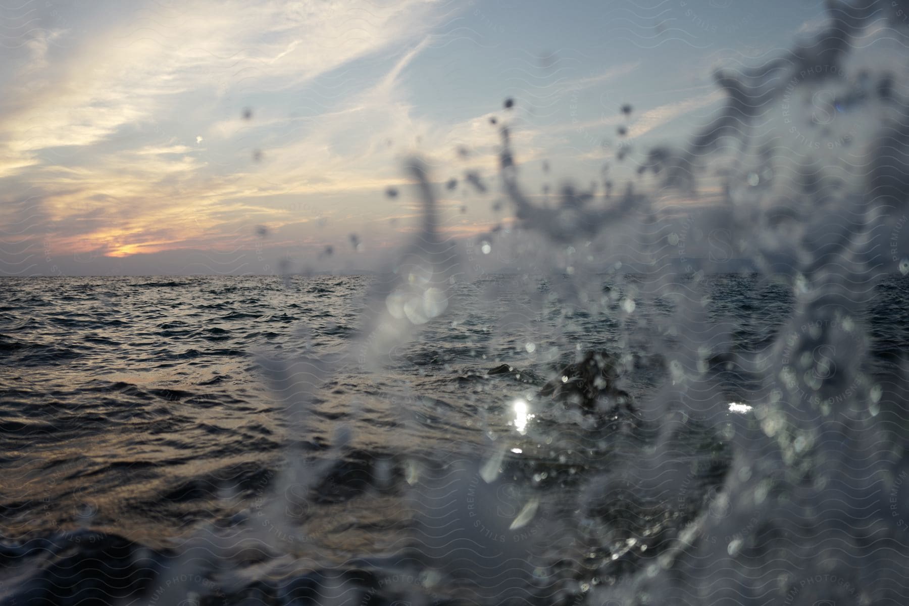 A wave crashes on a calm sea at sunset