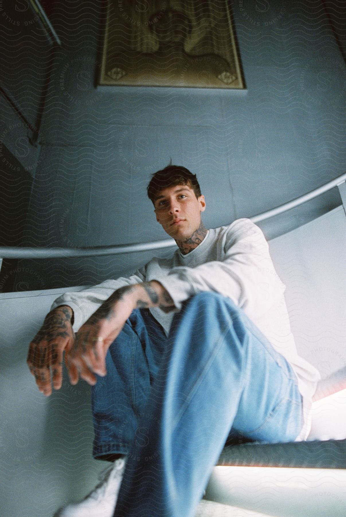 A young man covered in tattoos sits on a staircase his arms resting on his knees