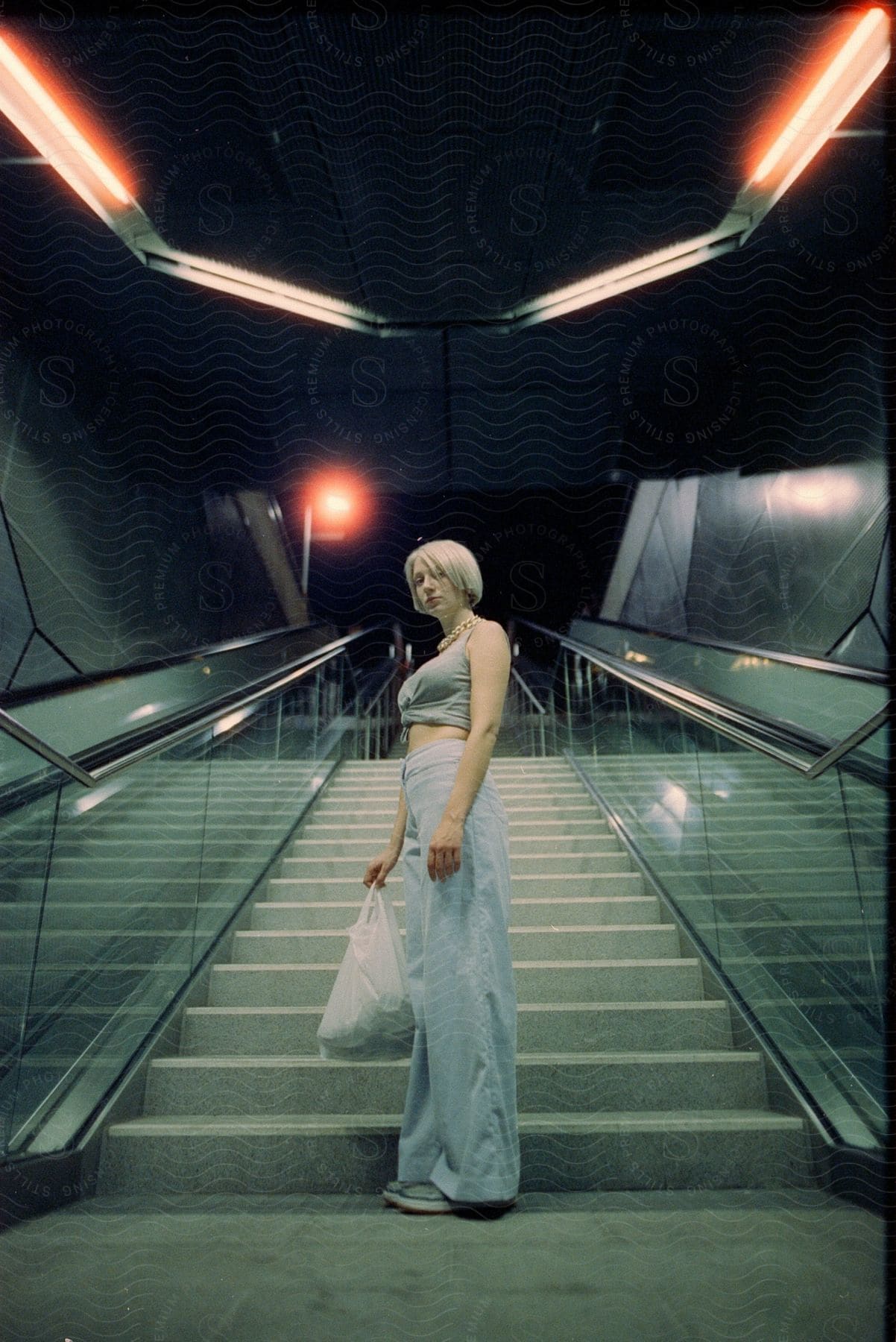 A person in a happy and carefree mood wearing a coat and holding a handbag is standing on a staircase with flash photography