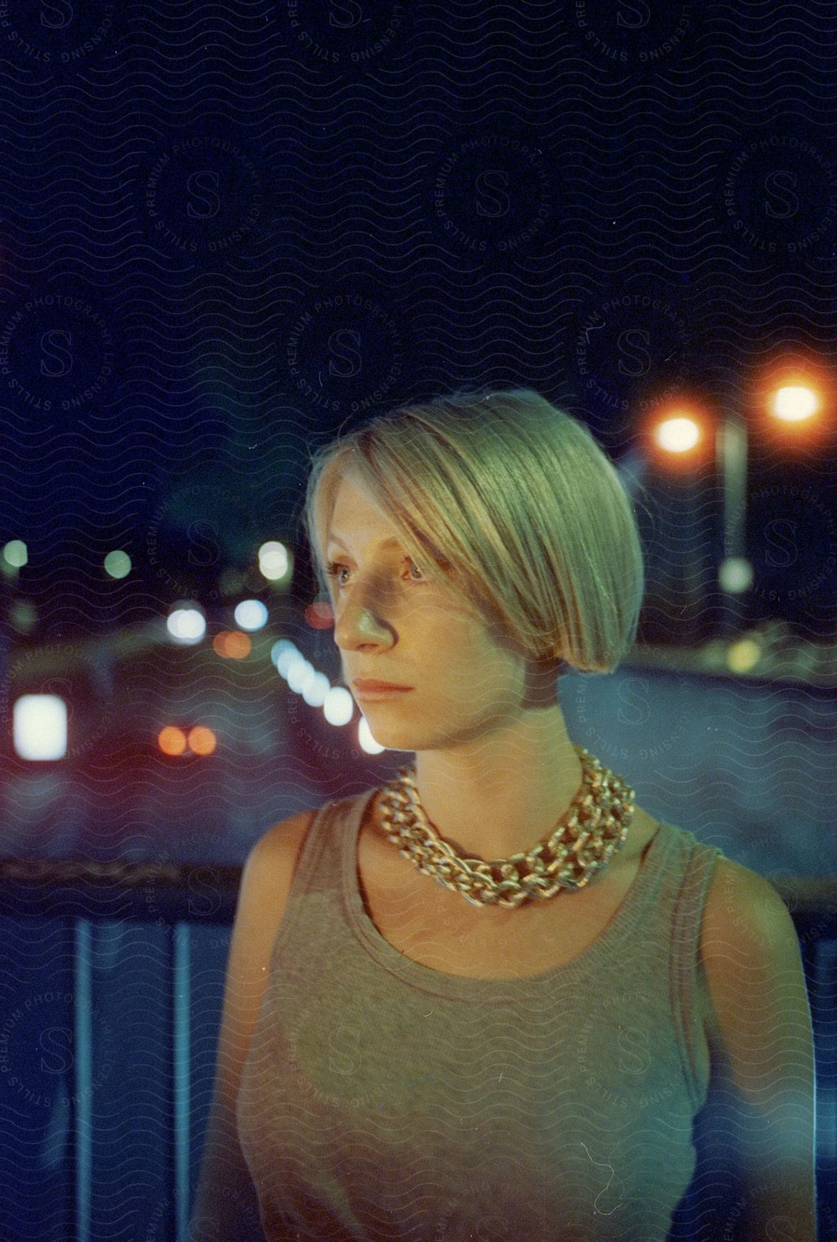 A lady standing by the roadside at night photographed in color with fast shutter speed and high key lighting