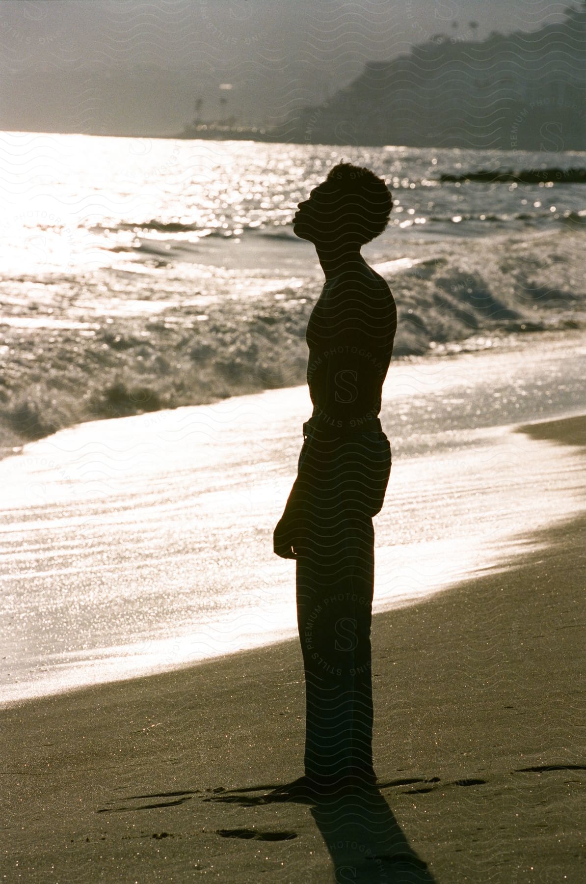 Black man standing next to the sea at the beach with hills and vegetation in the background