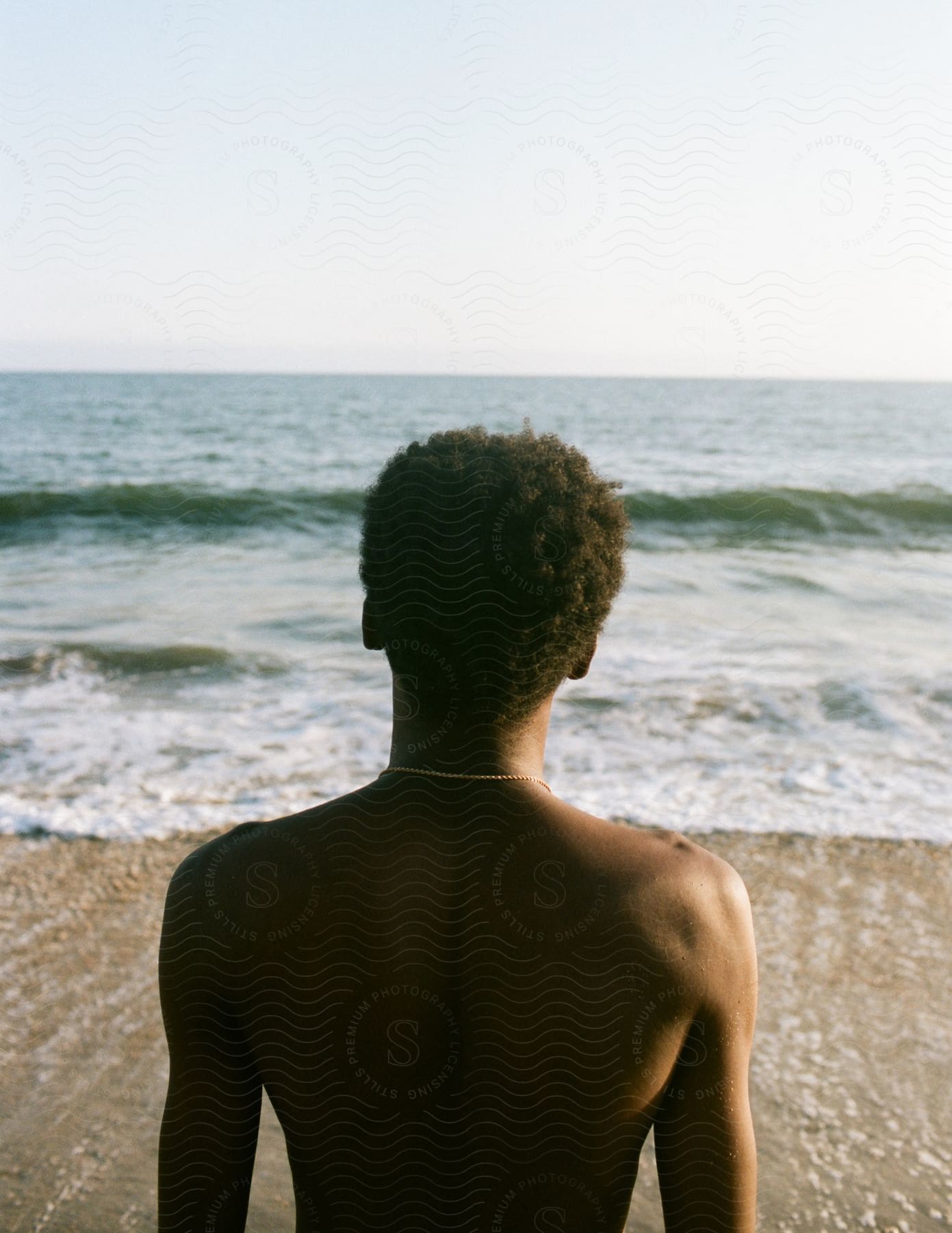 A man standing on the beach observing the rolling waves