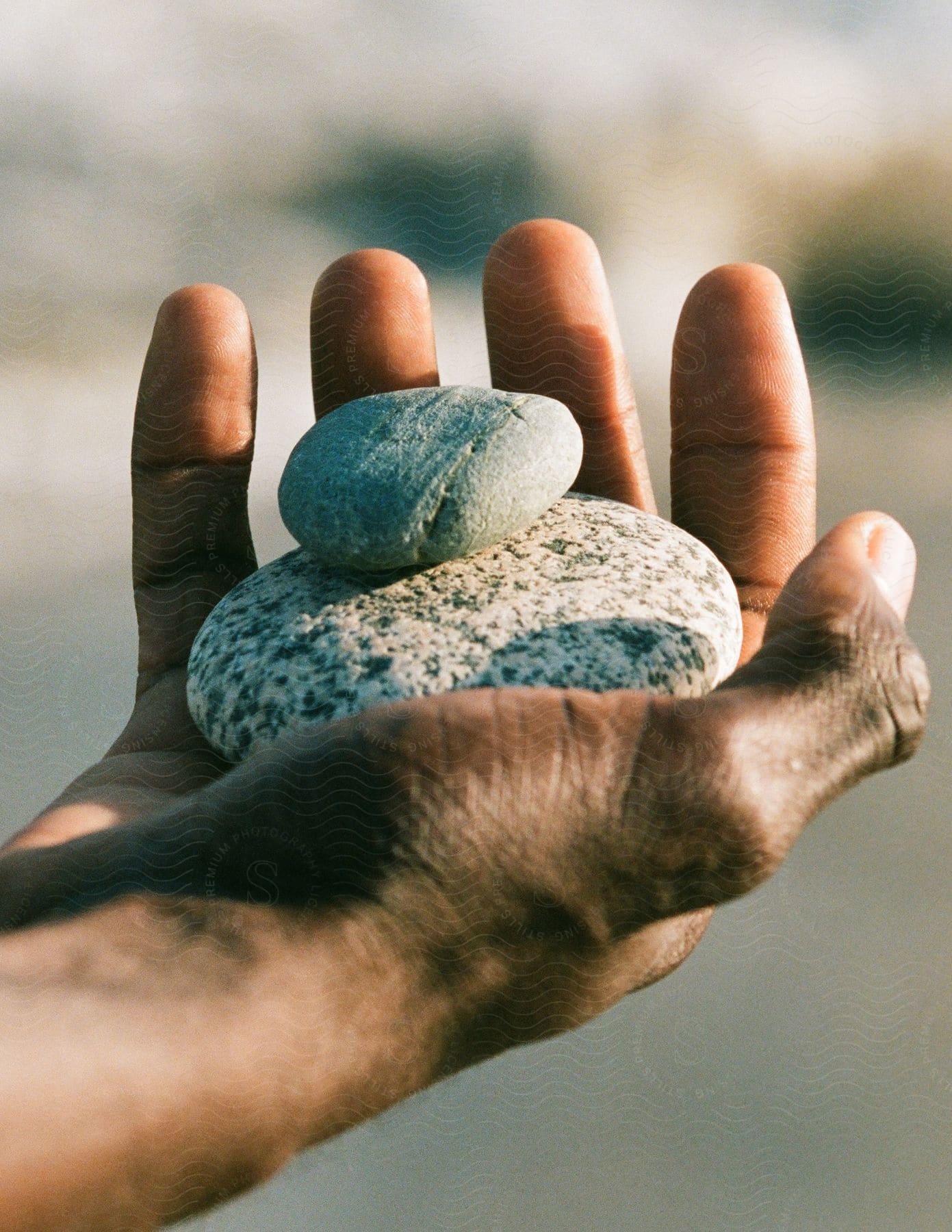 Mans hand holds two stacked oval stones
