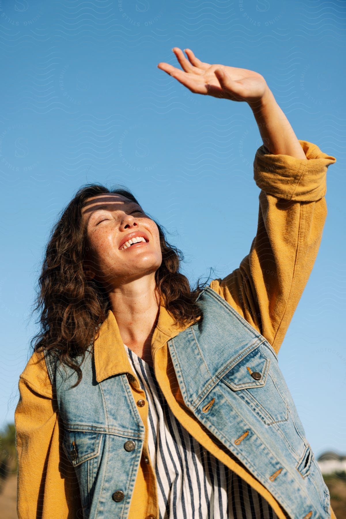 A woman in a coat laughing and raising her finger triumphantly against a sky backdrop