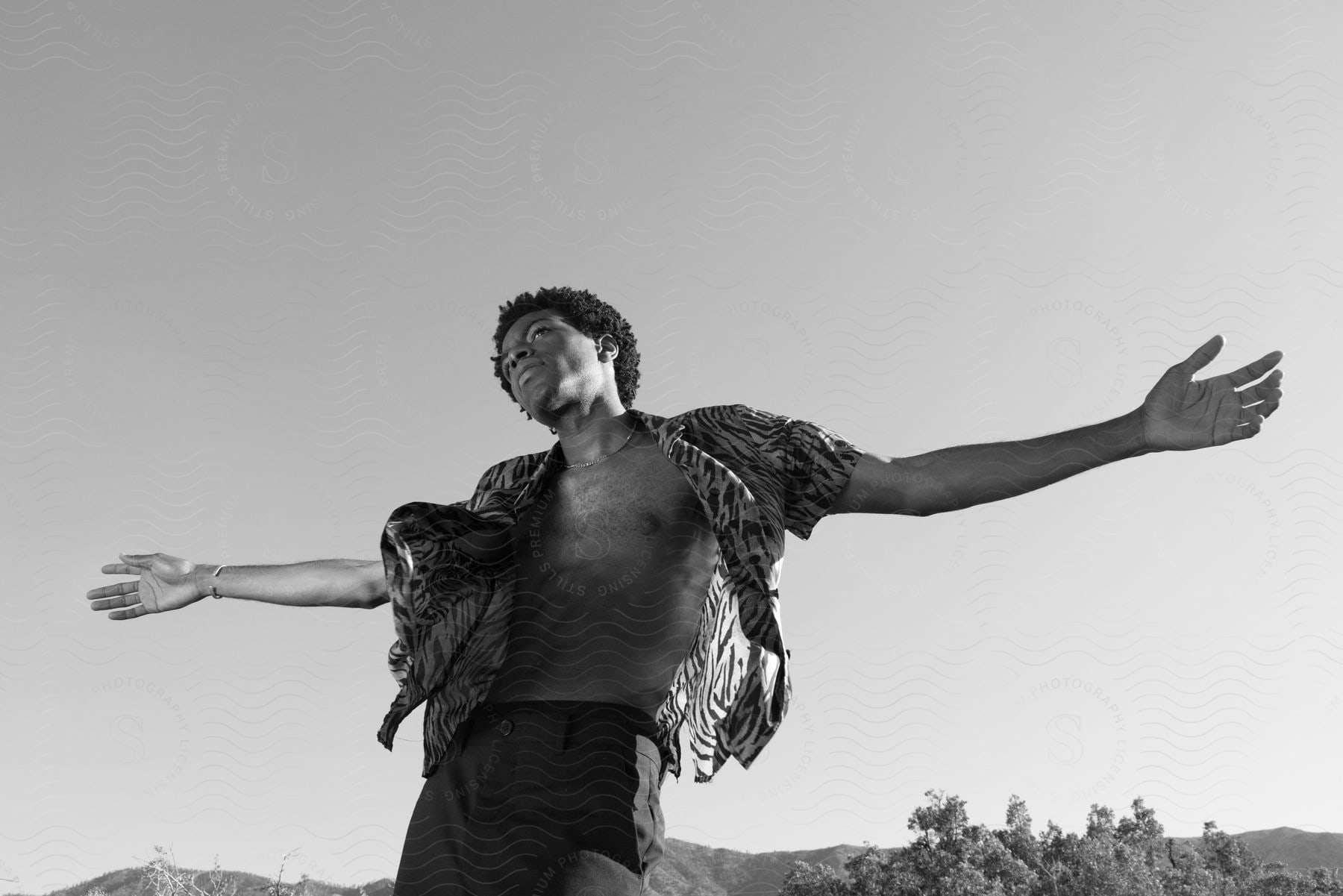 A person standing in the desert wearing shorts and a necklace with their arm raised in a happy gesture