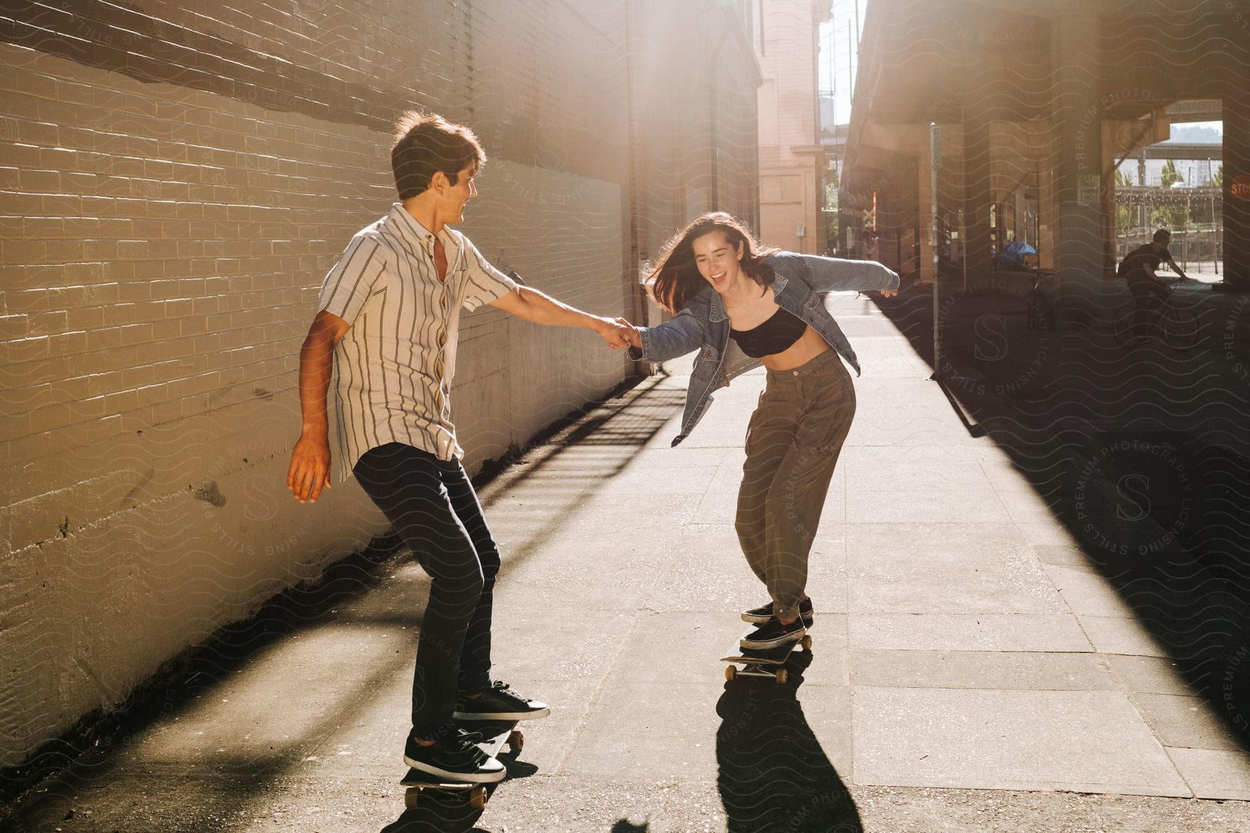 Stock photo of two people a boy and a girl holding hands and skateboarding in the city